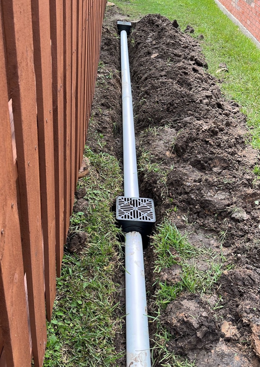 PVC drain line and catch basin installed along a fence line